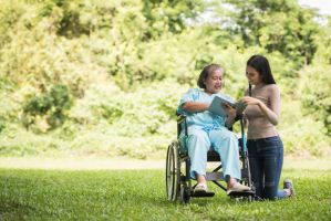 Happy Woman in a wheelchair reading a book with her daughter at the park
